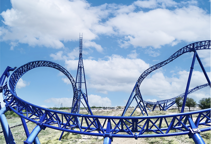 This is an image that captures the intricate design and structure of the ride in bright blue with white accents against a backdrop of a clear sky and distant trees, highlighting its complexity and beauty.